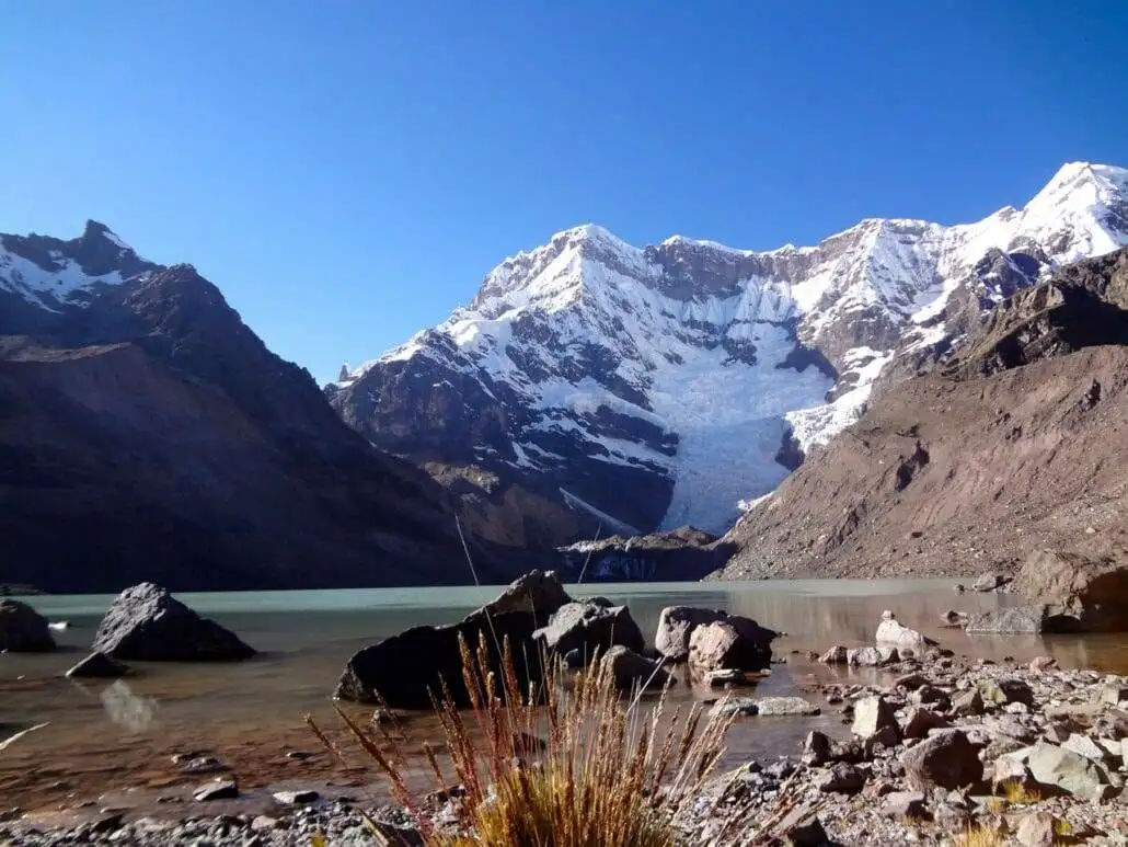 Apu Ausangate trekking reveals a picturesque lake encompassed by majestic mountains and rocks.