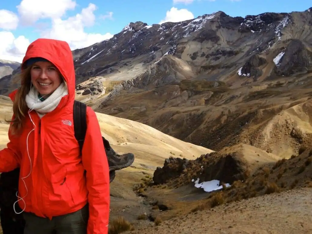 a woman in a red jacket trekking in front of mountains