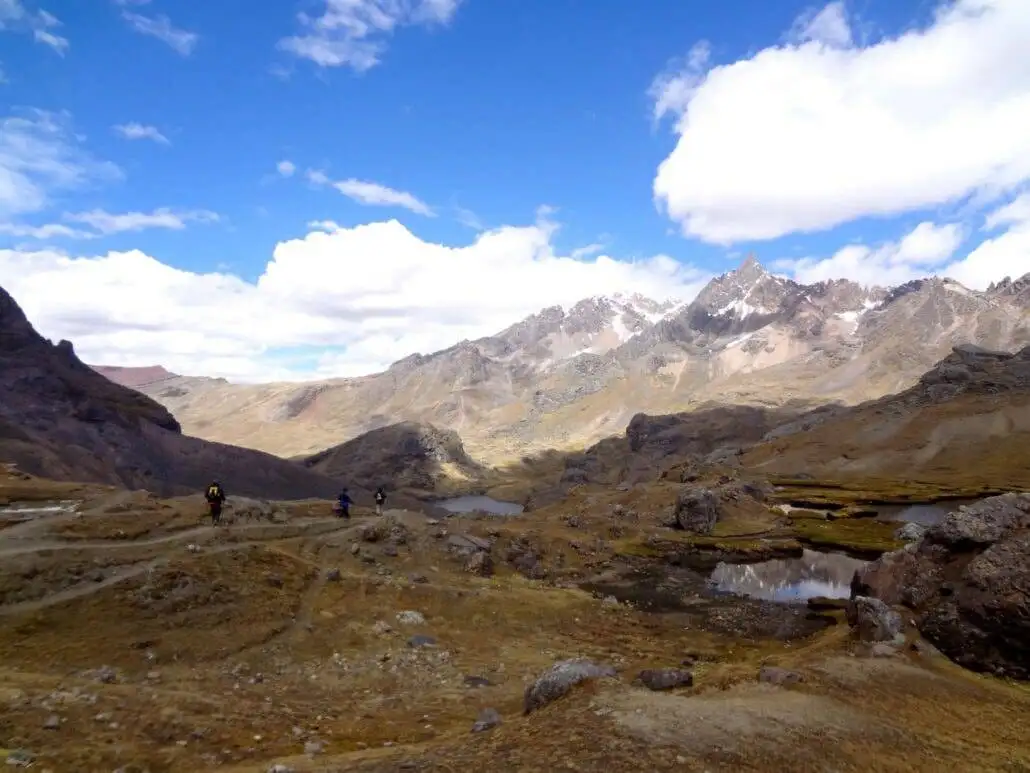 A group of people trekking in a valley with the Ausangate mountains as the backdrop.