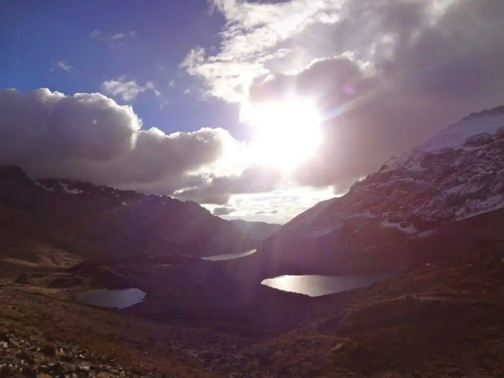 The sun is shining over a mountain lake during the Apu Ausangate trekking.