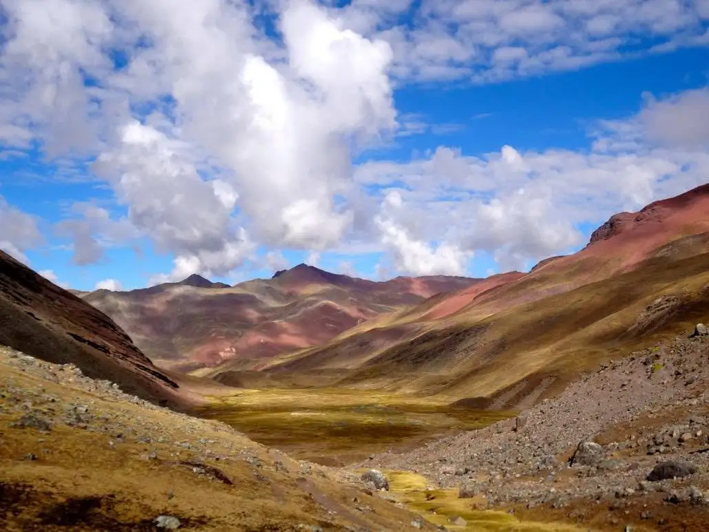 Apu Ausangate trekking trail, showcasing a valley with colorful mountains and a cloudy sky.
