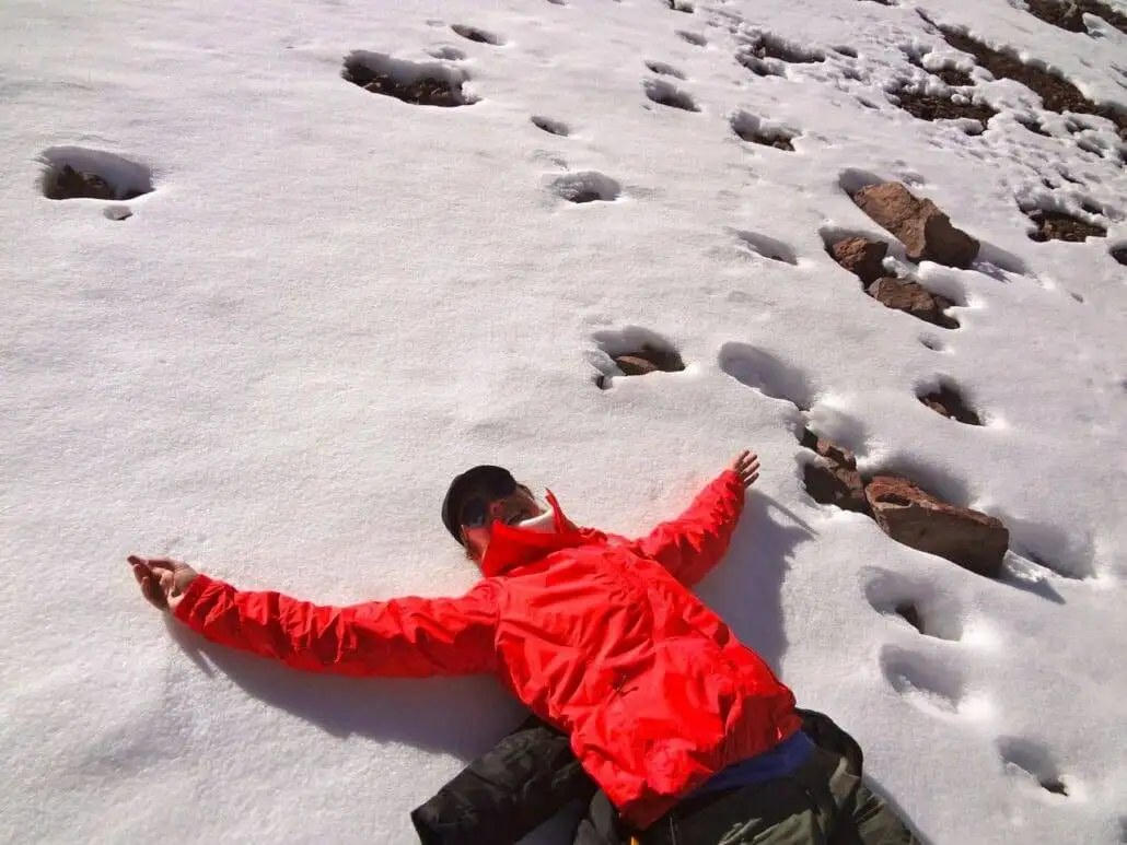 a man laying down in the snow, taking part in apu ausangate trekking with his arms outstretched.