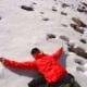 a man laying down in the snow, taking part in apu ausangate trekking with his arms outstretched.