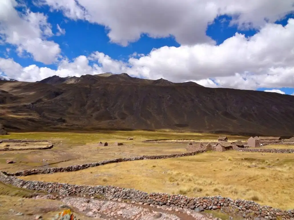 A small village in the middle of a field with mountains in the background, ideal for apu ausangate trekking.