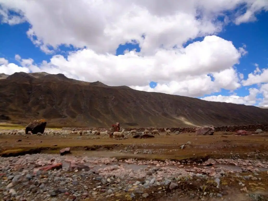 A man is hiking amidst rocky terrain with mountains in the backdrop during the Apu Ausangate trekking.