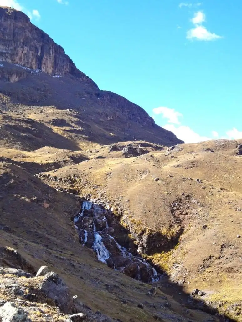 Apu Ausangate trekking adventure through a mountainous terrain with a picturesque stream.