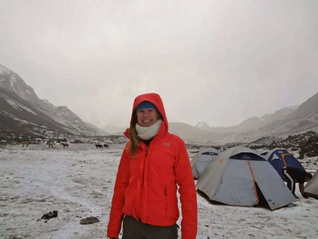a woman standing in front of tents during the Apu Ausangate trekking expedition in the snow.