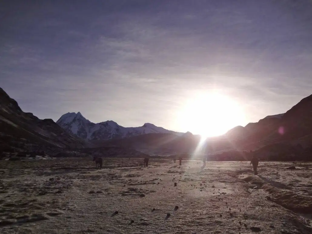 The sun is setting over a snowy area with mountains in the background during the Apu Ausangate trekking expedition.