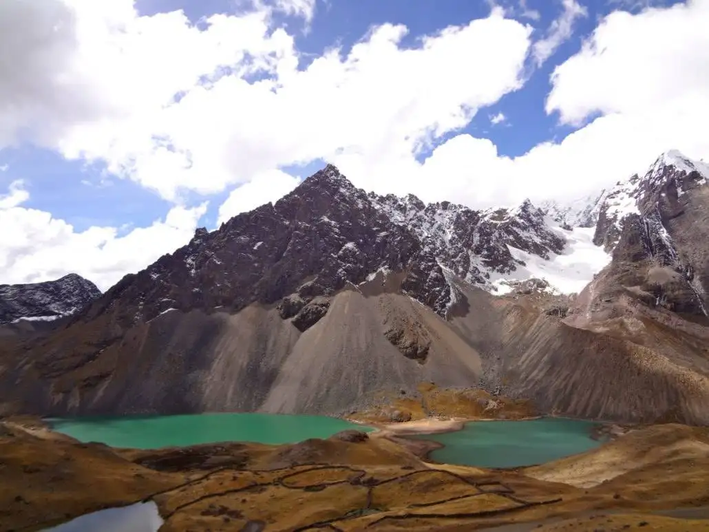 Apu Ausangate trekking leads to a stunning lake framed by mountains and clouds.