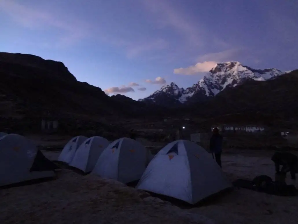 A group of trekkers set up campsites in the mountains at dusk during the Apu Ausangate trekking expedition.