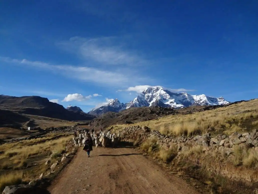 A group of people trekking along a dirt road with the spectacular Ausangate mountain towering in the background.