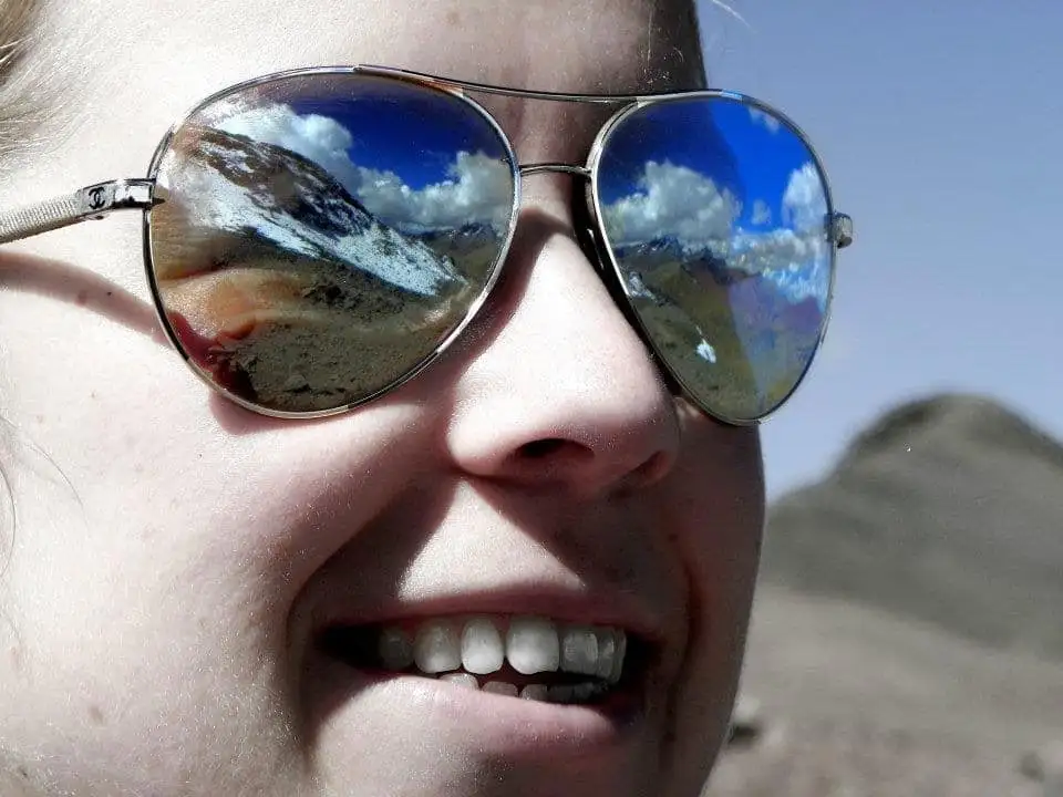 A woman trekking through Apu Ausangate dons sunglasses, reflecting the stunning mountain views.