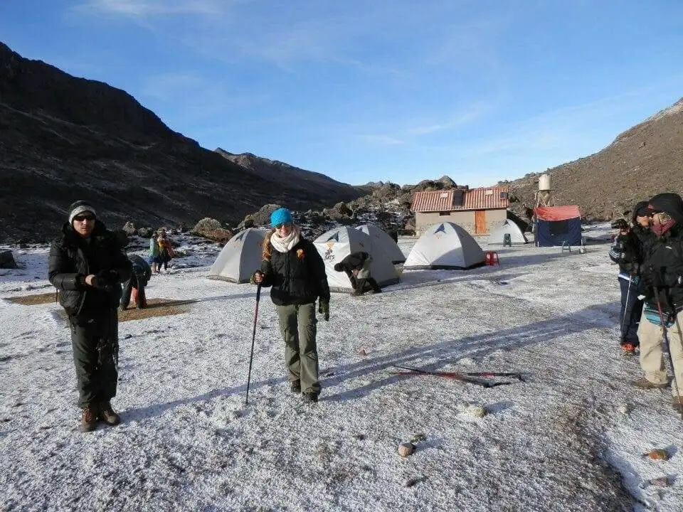 A group of people trekking in front of tents amidst snowy mountains.