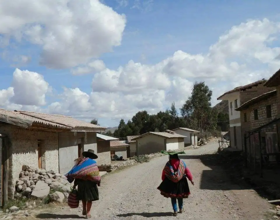 Two women trekking down a dirt road in a village during the Apu Ausangate trek.