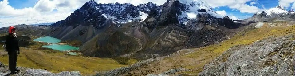A person trekking on Apu Ausangate overlooks a lake from the top of a mountain.