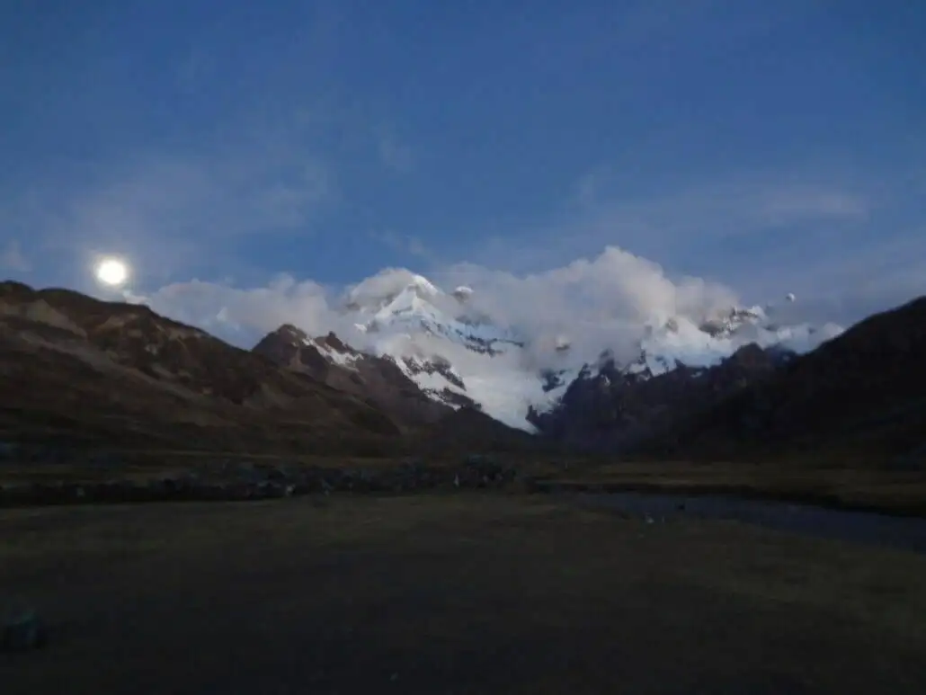 The moon rises over the Apu Ausangate mountain range at dusk.
