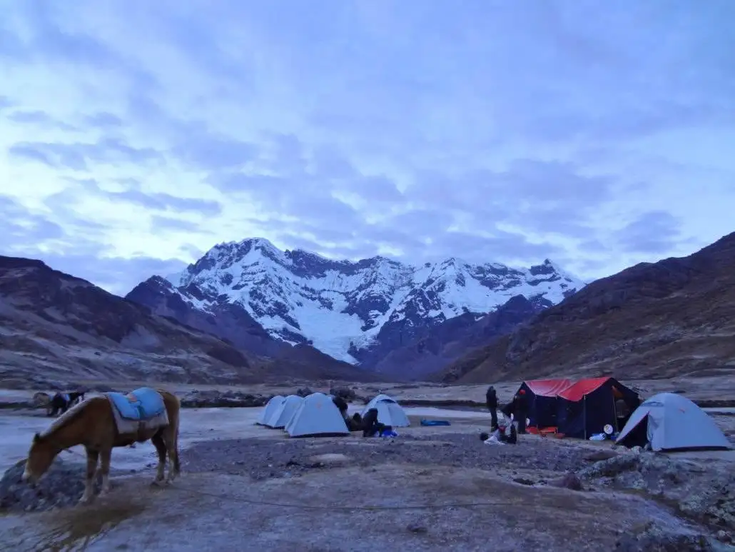 A group of people on the Apu Ausangate trekking adventure standing near tents in front of a mountain.