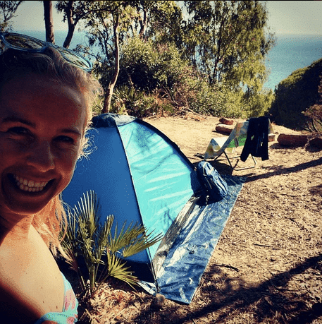 a woman in a bikini standing in front of a tent for a mountain warehouse review.