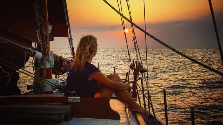 a woman sitting on the deck of a sailboat at sunset.
