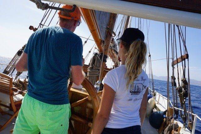 A couple stands on the steering wheel of a sailboat, embracing the oceanic nomadic lifestyle.