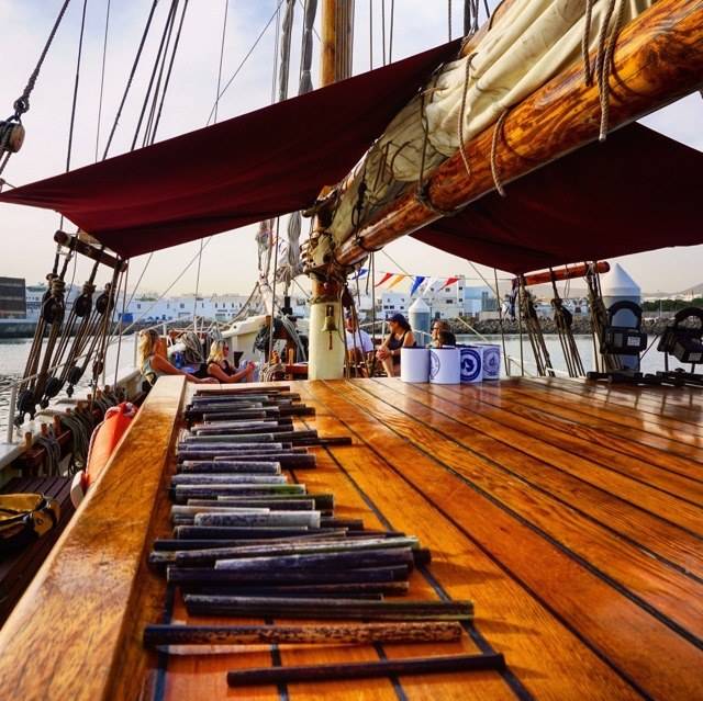 The deck of a tall ship floating on the ocean with nomads sitting on it.