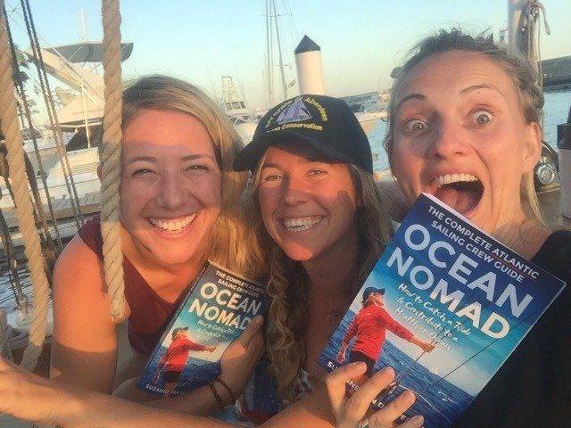 Three women on a boat proudly showcasing their Ocean Nomad books.