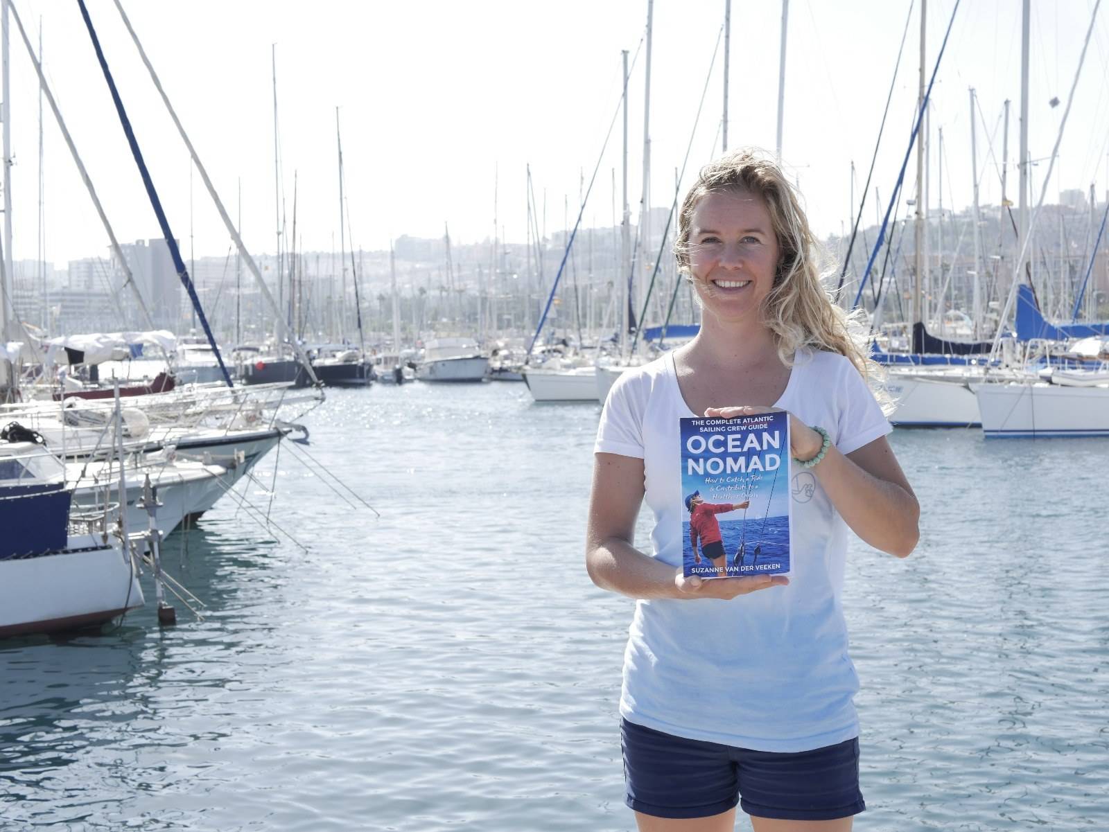 A nomadic woman holding an Ocean book in front of a marina.