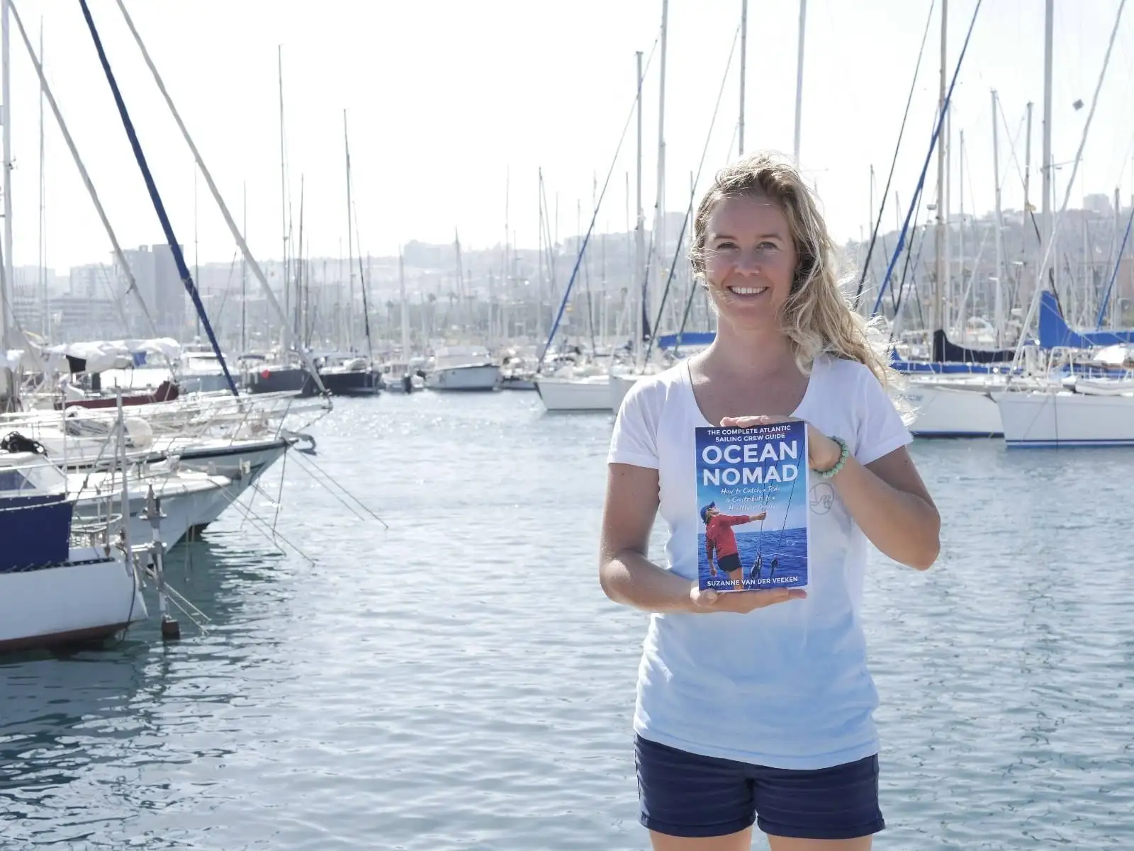 A nomadic woman holding an Ocean book in front of a marina.