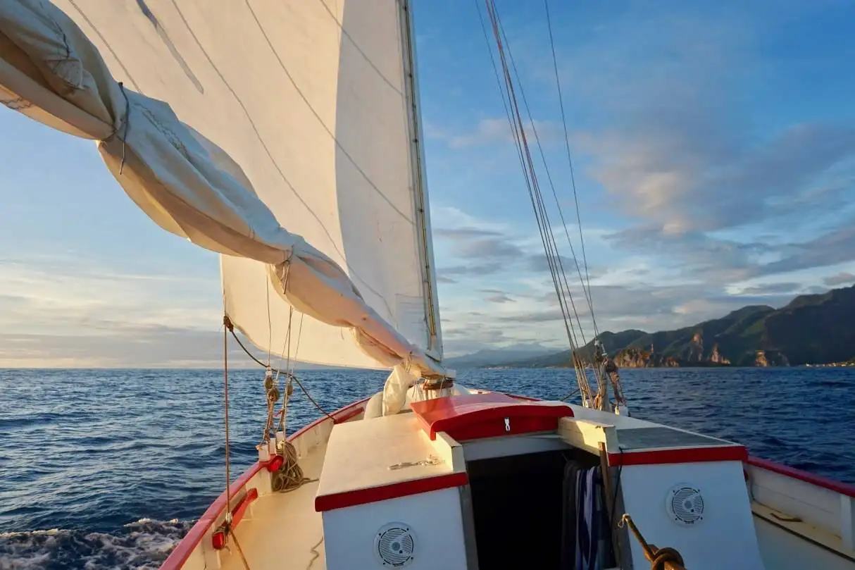 a sailboat in the ocean with mountains in the background.