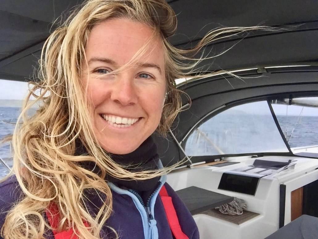 a woman smiling in the cockpit of a sailboat.