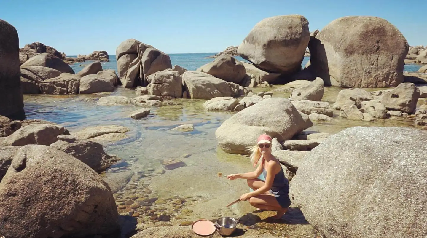 A woman sitting on a rock in the water washing with biodegradable soap.
