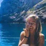 a woman smiles while sipping coffee on a boat.