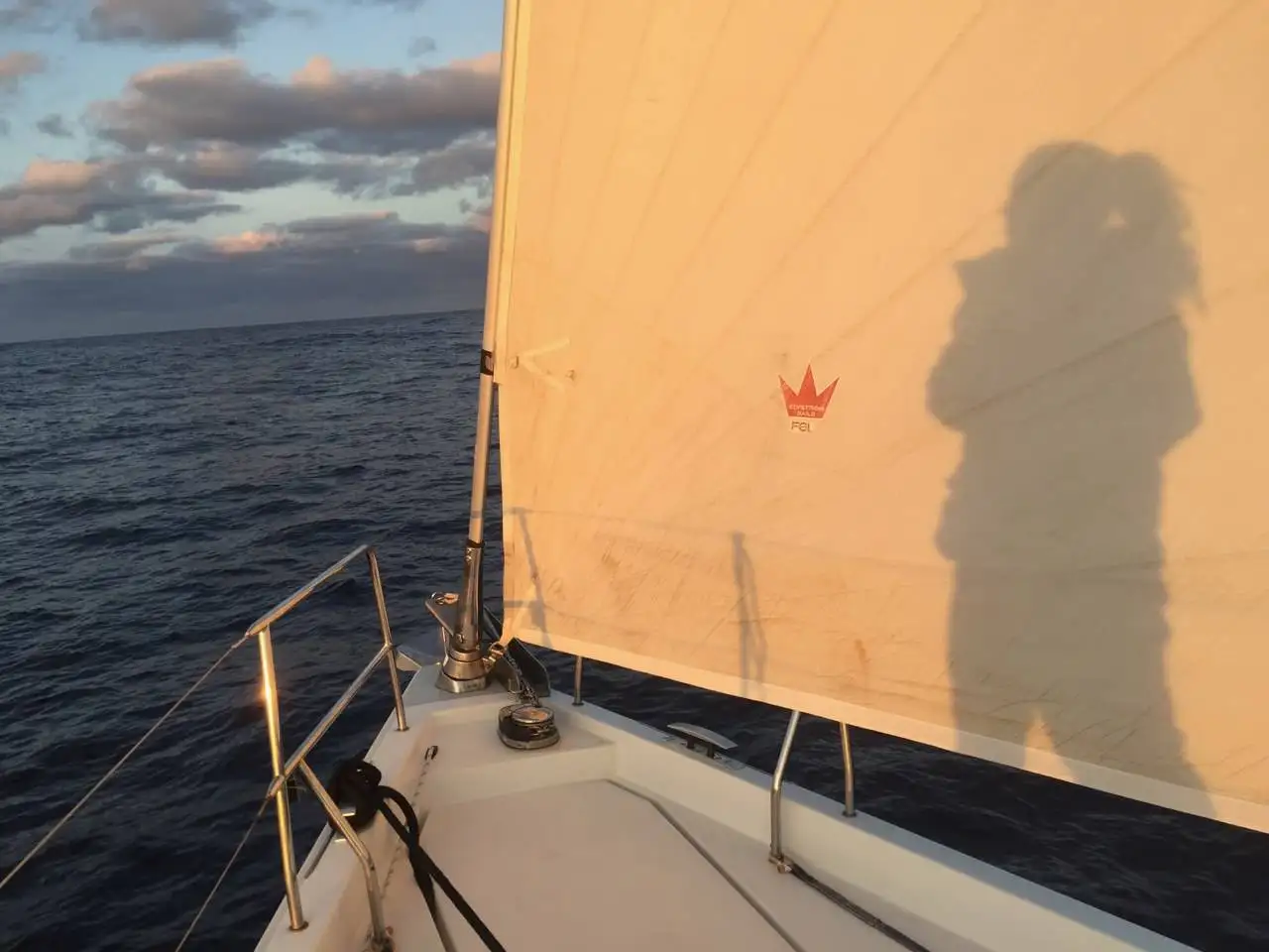 A person standing on the bow of a sailboat, equipped with offshore sailing gear.
