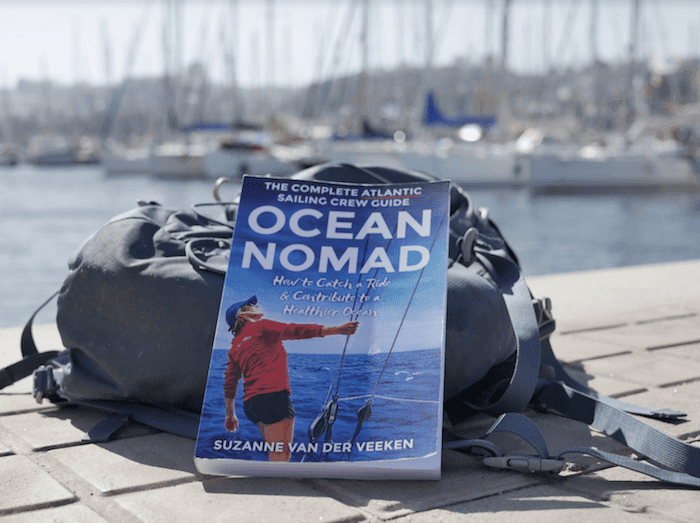 The book "Ocean Nomad" is sitting on a bench near a boat, surrounded by offshore sailing gear.
