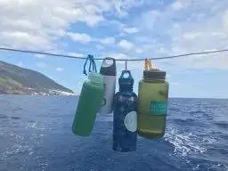 Offshore sailing gear including water bottles hanging on a rope on a boat.