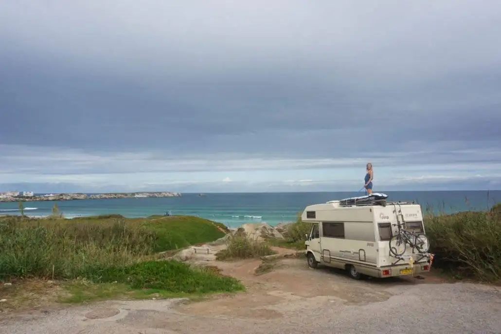 a camper parked on a dirt road next to the ocean.