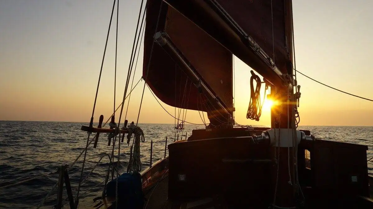 a sailboat in the ocean with the sun setting behind it.