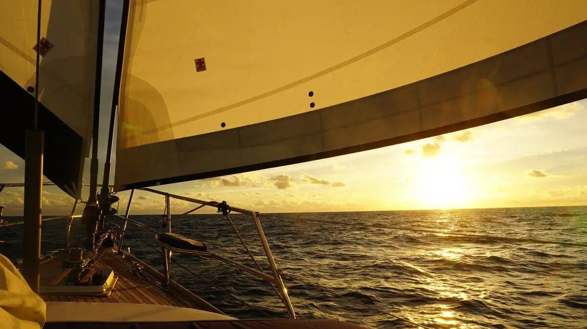 a sailboat in the ocean with the sun setting behind it.