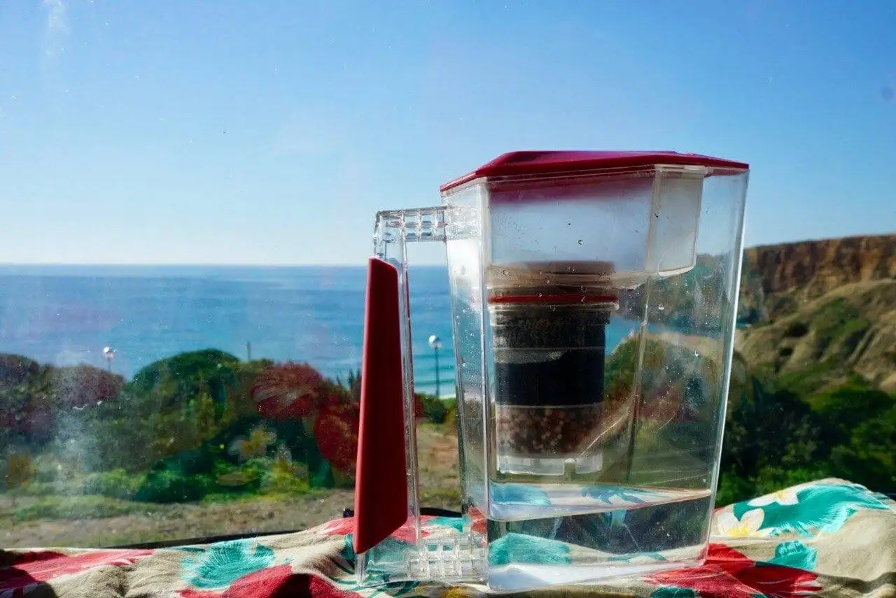 A portable coffee maker with a built-in water filter sitting on a table overlooking the ocean.