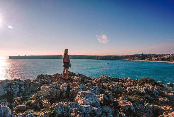 A woman perched on a rock enjoying the panoramic view of the ocean in Coliving Algarve.