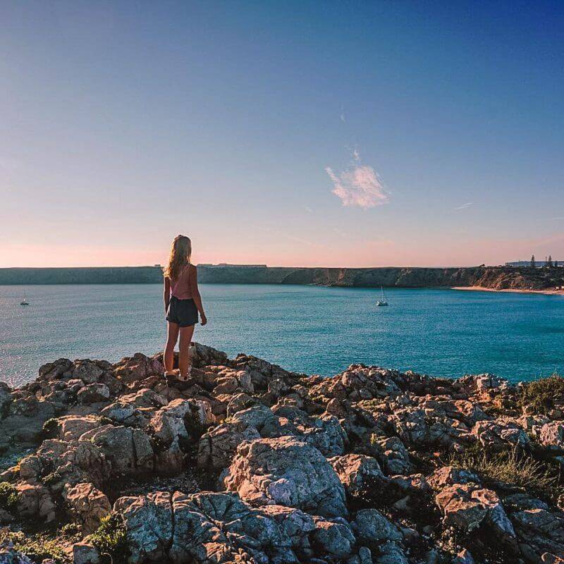 A woman perched on a rock enjoying the panoramic view of the ocean in Coliving Algarve.