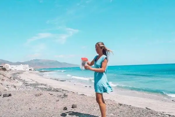 a woman in a blue dress standing on a beach, carrying a travel water filter.