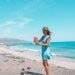 a woman in a blue dress standing on a beach, carrying a travel water filter.