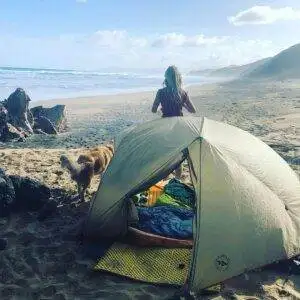 a woman standing next to a tent on the beach.