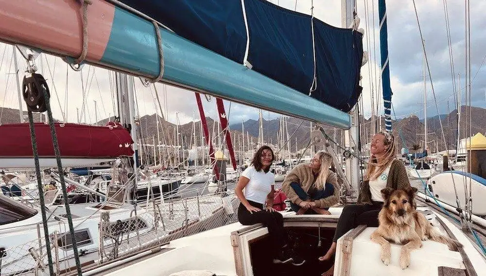 three women sitting on the deck of a sailboat with a dog.