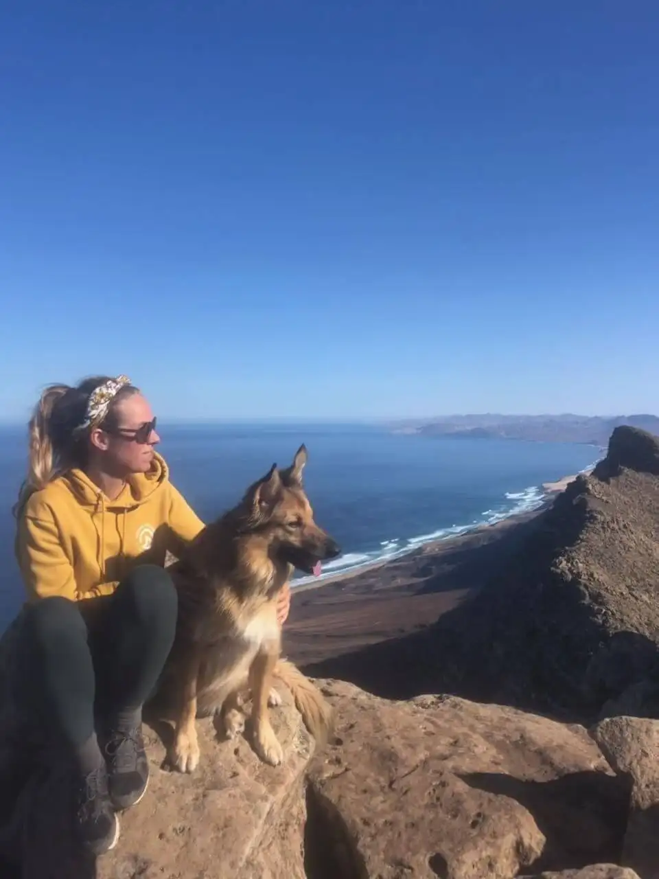 a woman sits on top of a mountain with her dog.