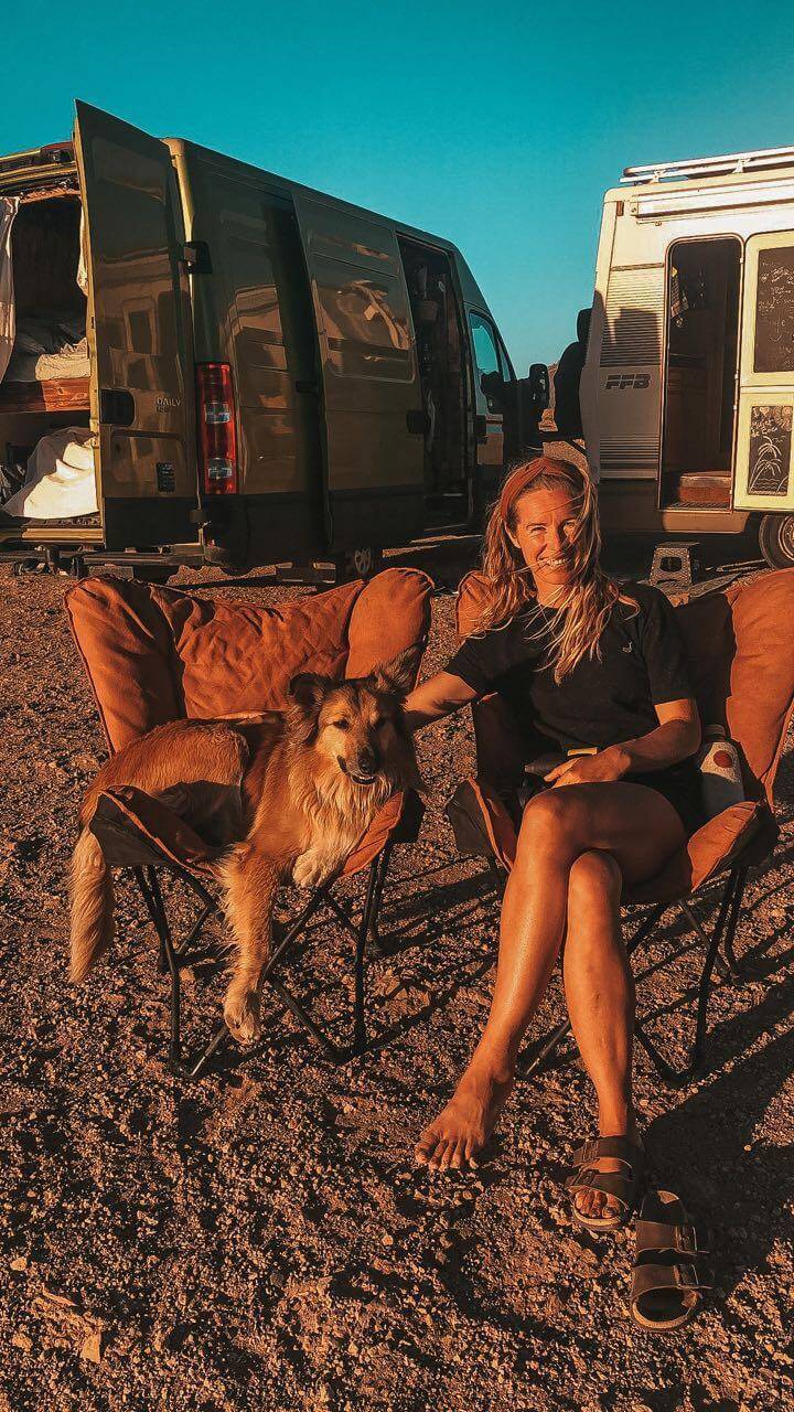 a woman sits in a chair next to an rv in the desert.