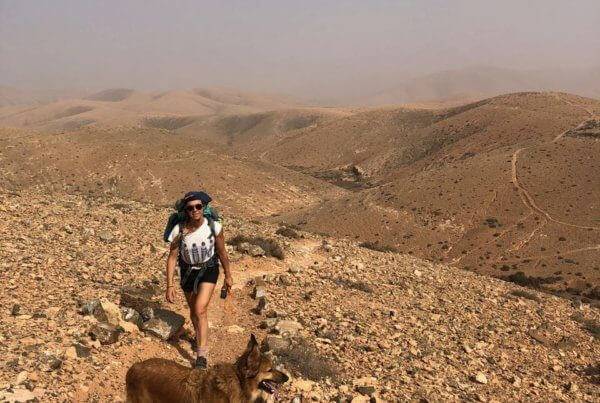 a woman hiking with a dog in the desert.