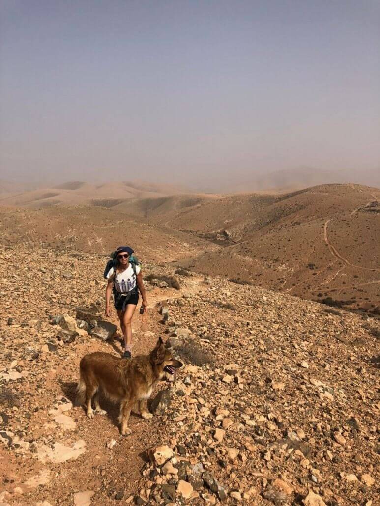 a woman hiking with a dog in the desert.