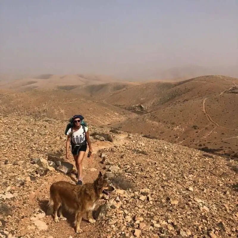a woman hiking with a dog in the desert.